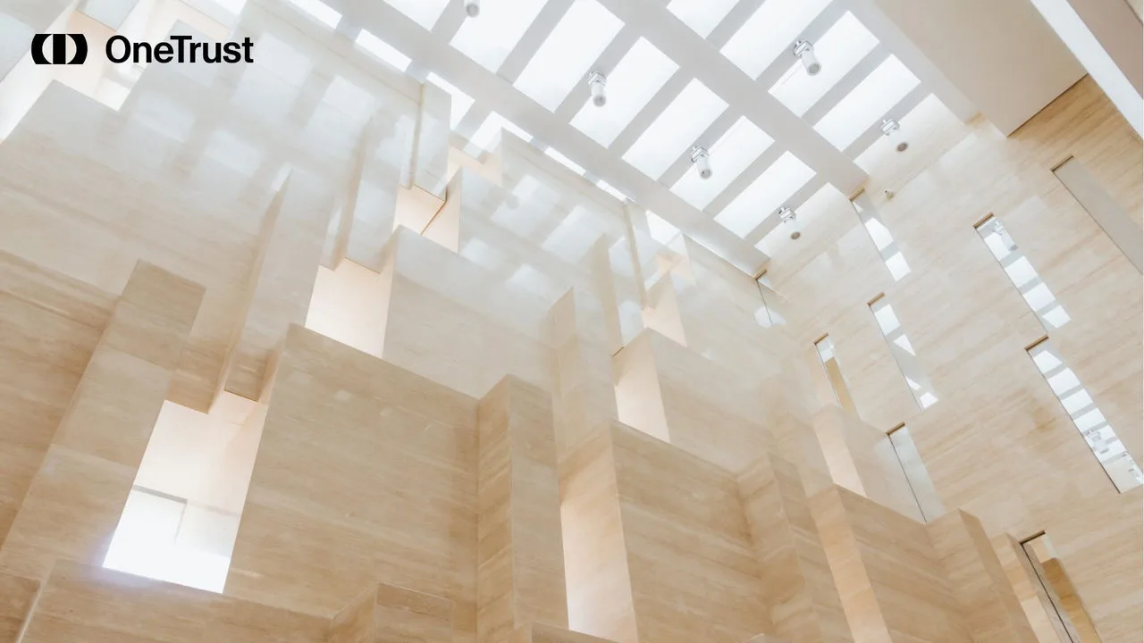 Bright modern atrium with cream stone walls, skylights, and a black OneTrust logo in the upper-left corner.