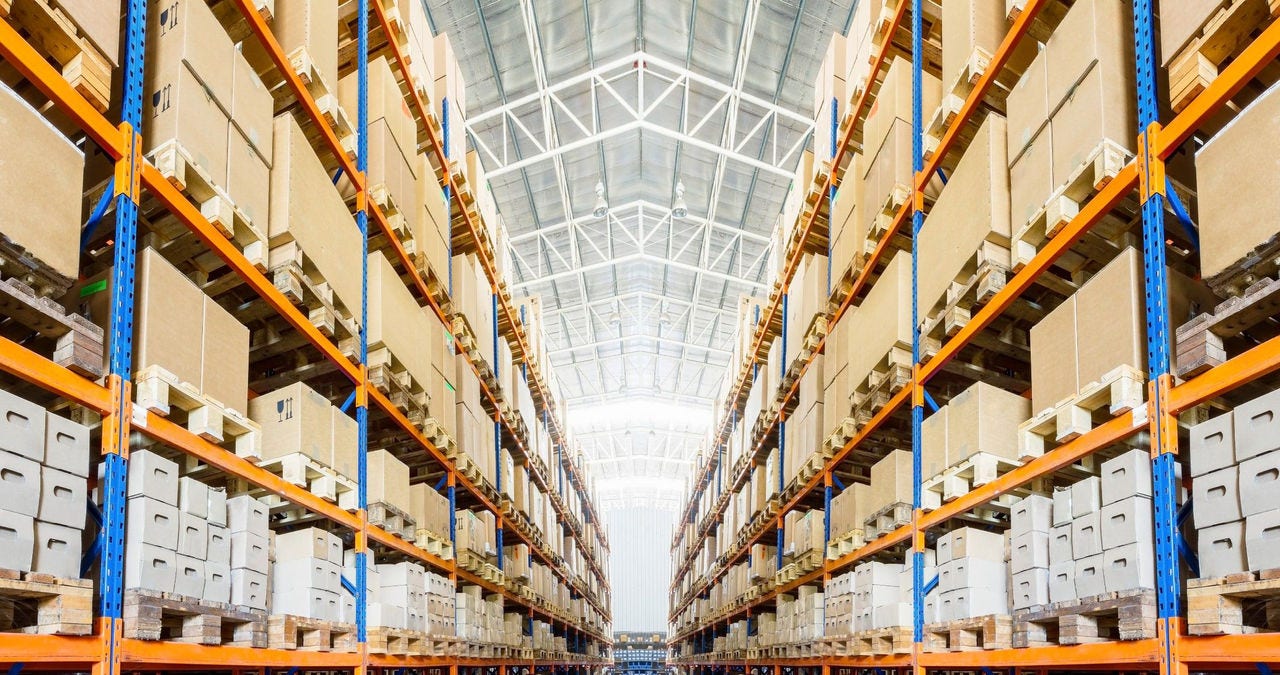 The inside of a giant shipping facility and an wide aisle with many boxes on the shelves