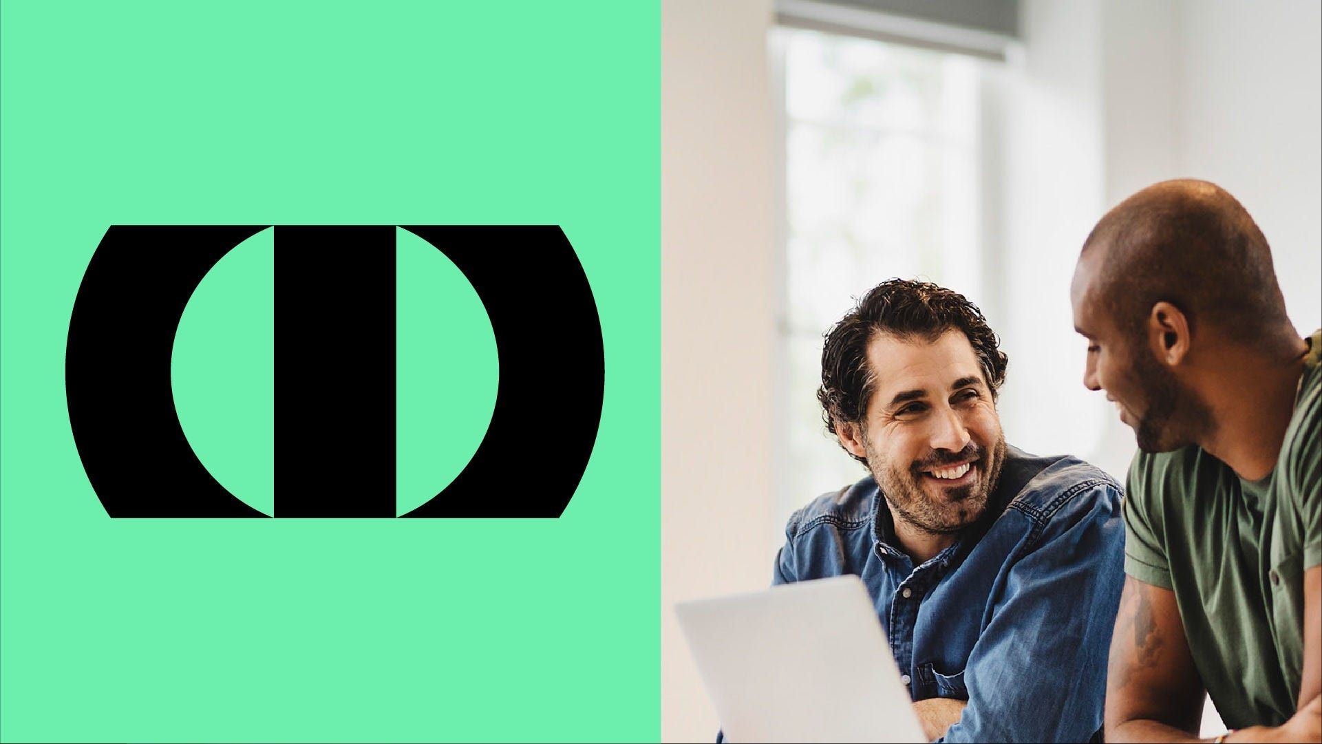 Two coworkers collaborating at a desk, reviewing content on a laptop in a bright office setting.