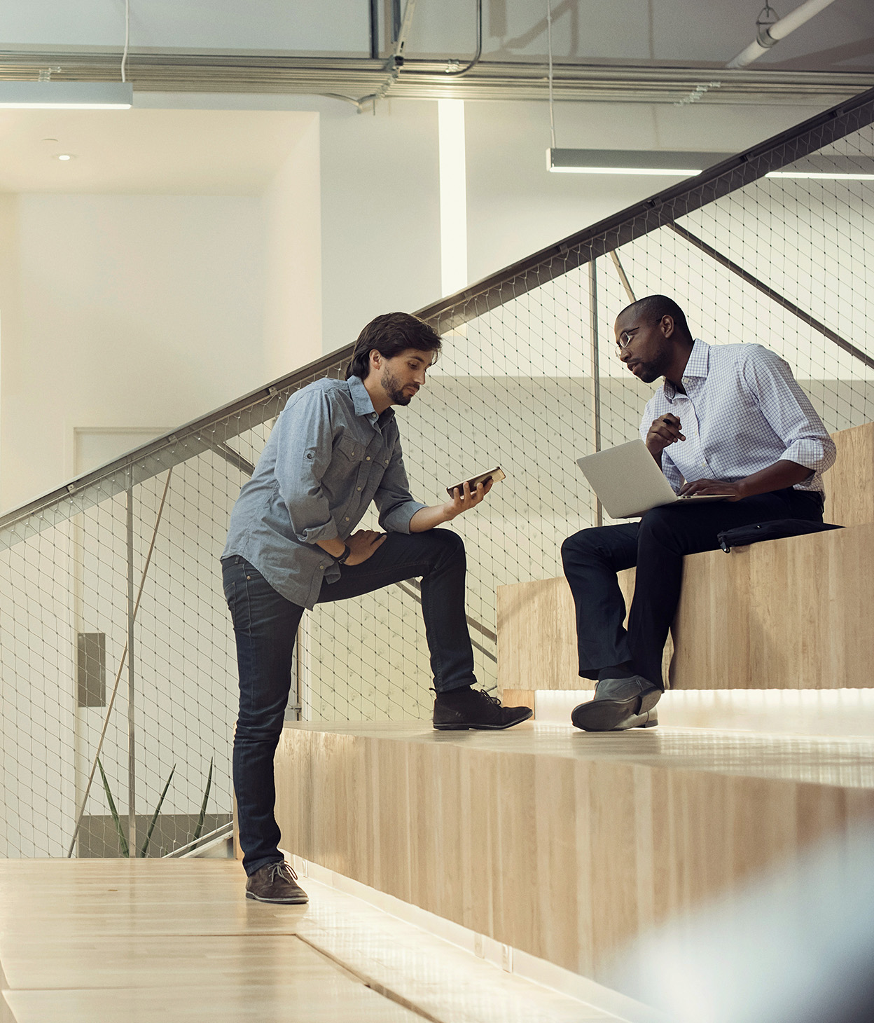 photo of two coworkers having a conversation on bleachers inside of an office presentation room.