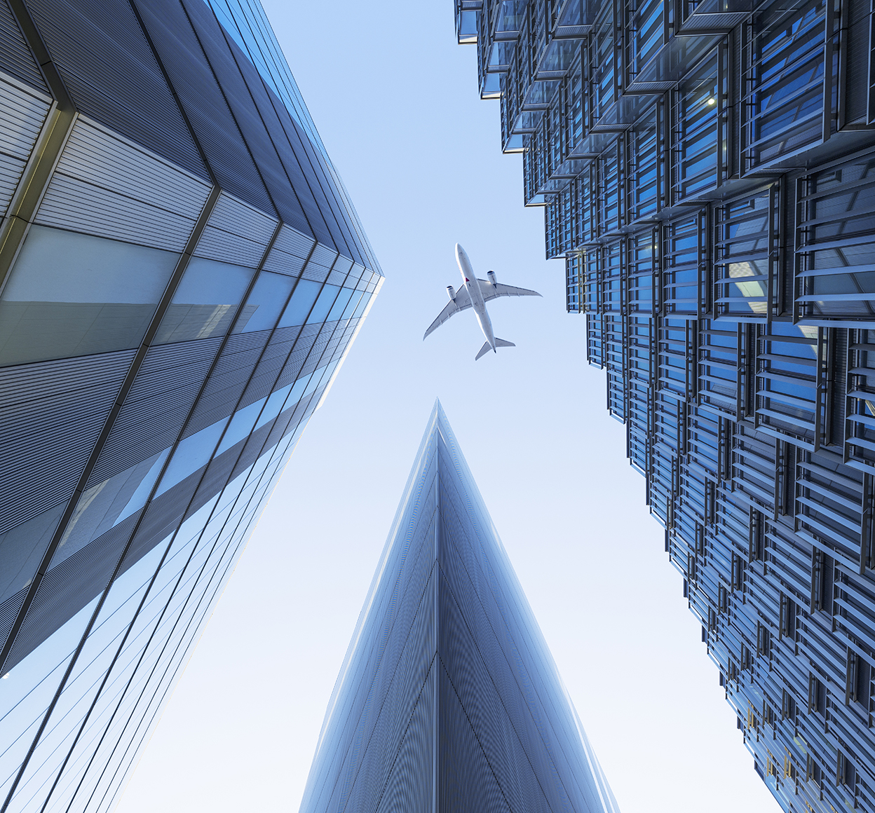 Blick von unten auf ein Verkehrsflugzeug, das über eine Gruppe von Wolkenkratzern fliegt