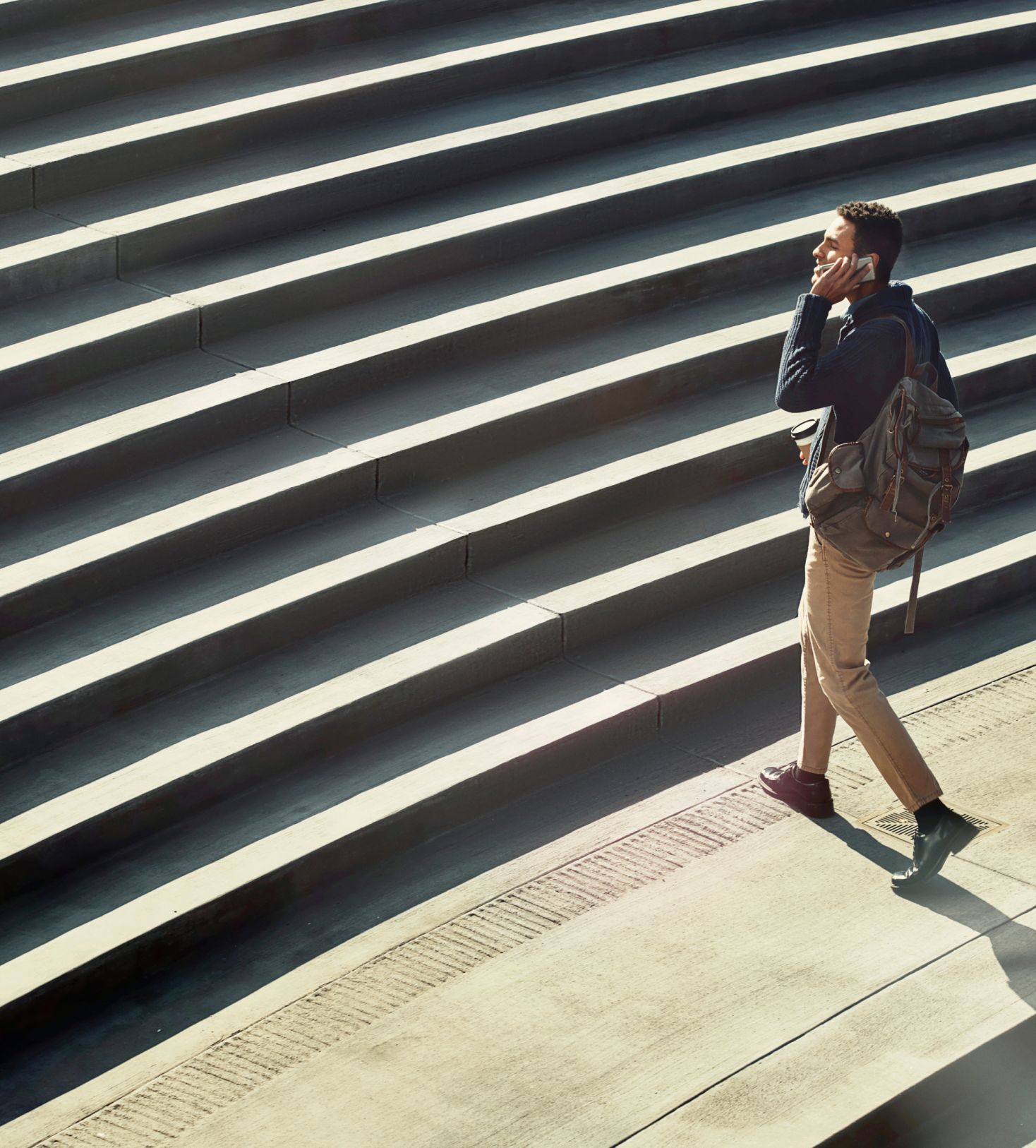 Photo of a man with a cellphone and backpack climbing a set of stone stairs